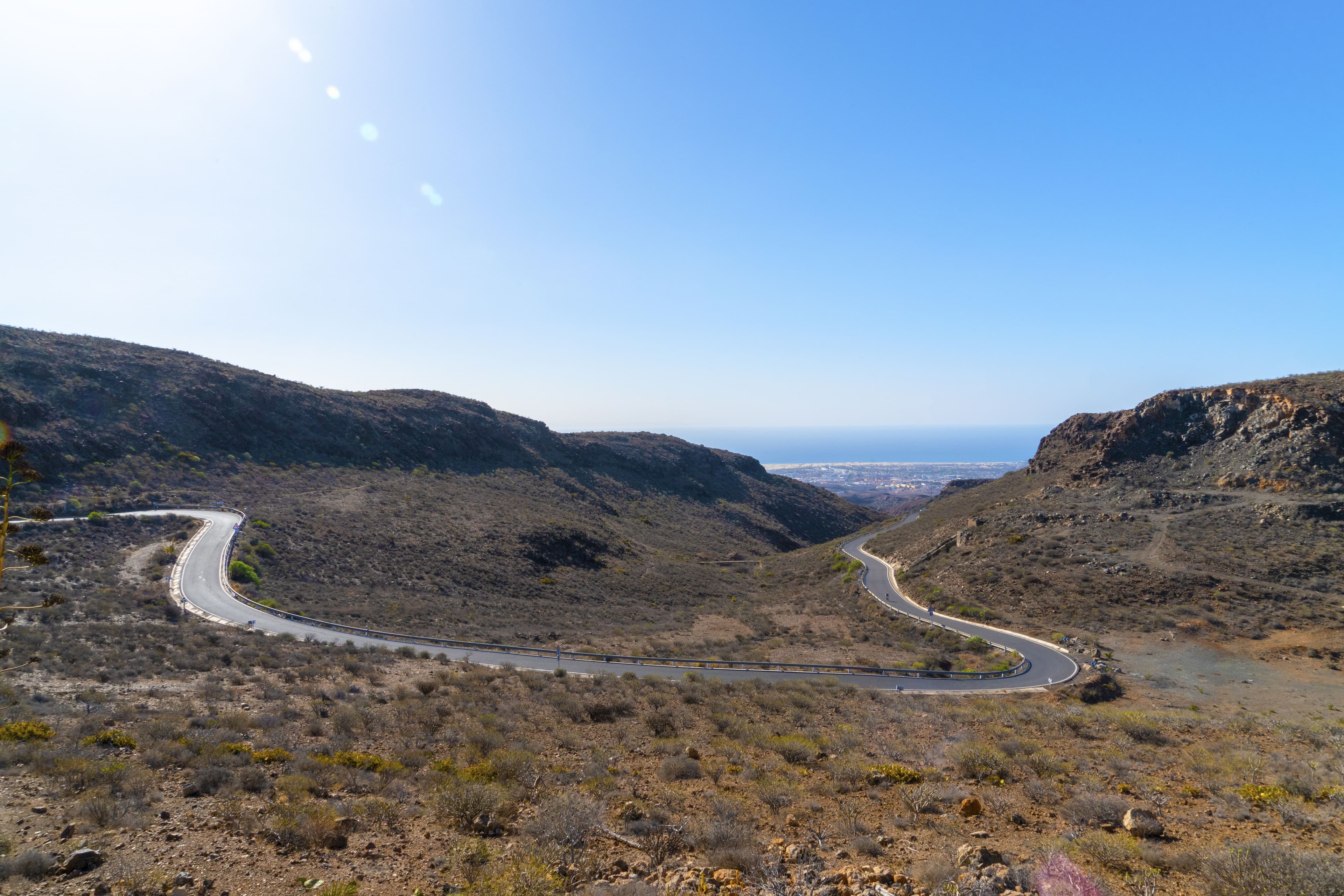 An empty road curving through arid hills toward the south coast
