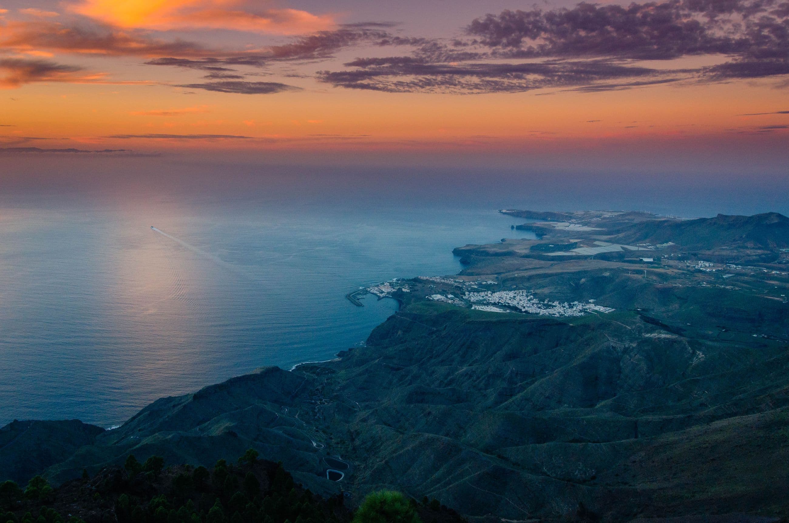 Gran Canaria's coast at dusk from above, roads threading down to a lit town and the sea